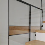 Posuvné dveře Mline - černý komaxitový rám v kombinaci s bílým matným sklem Matelac (RAL 9003), pruhy ze dřeva použitého na podlaze